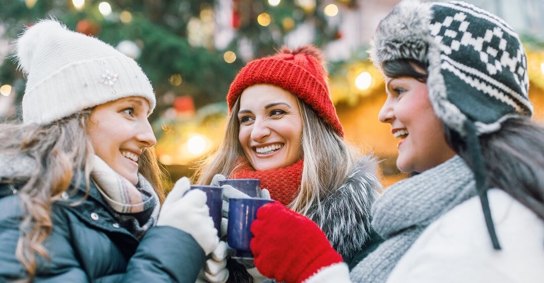 Three women at a Chirstmas market wishing each other Merry Christmas in German