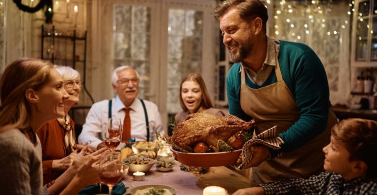 Happy,Man,Bringing,Roast,Turkey,At,The,Table,During,Thanksgiving