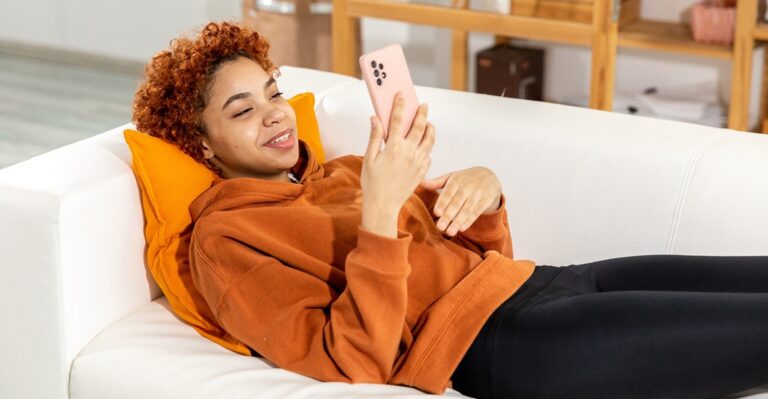 Smily, African woman laying on a couch with her phone to research the best websites to learn French